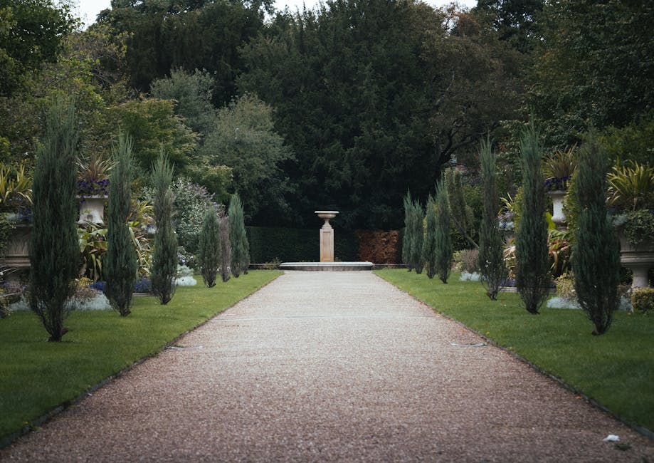 A traditional brick residential building with white-framed windows and a curved bay window on the upper floor, set against a partly cloudy sky. The garden features a stone pathway leading to the entra